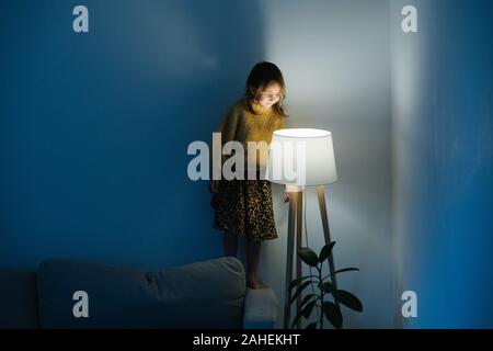 Kleines Mädchen in Pullover steht auf einer Couch an nigth Licht zu Hause suchen. Stockfoto