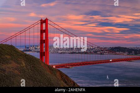 Panorama von der Golden Gate Bridge bei Sonnenuntergang mit Marin Headlands im Vordergrund, San Francisco Skyline und bunten Wolken im Hintergrund Stockfoto