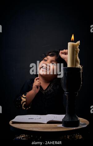 Kleines Mädchen schreiben Hausaufgaben bei Kerzenschein in der Nacht Stockfoto