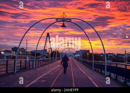 Southport, Merseyside, UK. 29. Dezember, 2019. Rayleigh-streuung; der Himmel war blutrot heute morgen als die Sonne stieg in Merseyside. Menschen zu Fuß auf der Pier intensiven feurigen Winter rot und orange Himmel in der Dämmerung als Sonne in Southport genießen, Roter Himmel am Morgen, Shepherd's Warnung' erscheint zuerst in der Bibel im Buch von Matthew. Es ist eine alte Wetter oft bei Sonnenaufgang verwendet, die sich wandelnden Himmel zu bedeuten und wurde ursprünglich bekannt zu helfen, für das Wetter für den nächsten Tag vorzubereiten. Credit: MediaWorldImages/AlamyLiveNews. Stockfoto