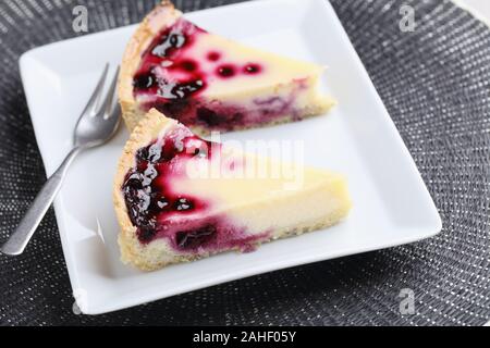 Zwei Scheiben von schwarzen Johannisbeeren Käsekuchen auf einem weißen rechteckigen Platte Stockfoto