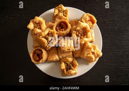 Traditionelle östliche sortierten Baklava. Ansicht von oben. Arabisch gebackene Süßigkeiten in weiße Platte auf dunklen Holztisch. Baklawa Mischung Stockfoto