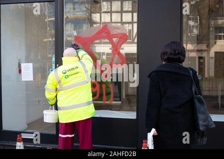 Ein Rat Reiniger entfernt antisemitischen Schmierereien, die in Form von Zahlen, 9, 11, und David Stern, auf ein Schaufenster in Belsize Park, nördlich von London. Stockfoto