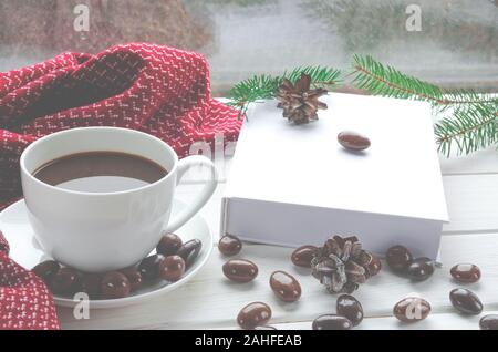 Weihnachten Konzept: Eine weiße Tasse Kaffee steht auf einem weißen Tisch neben einem weißen Buch öffnen und bunten Süßigkeiten vor dem Hintergrund einer Stockfoto