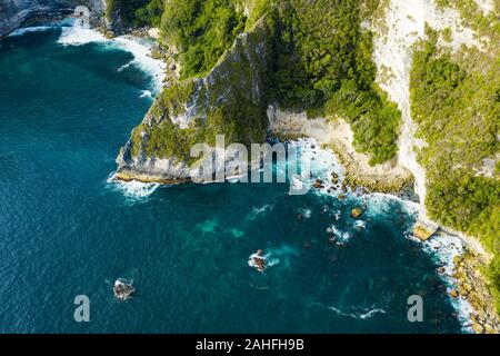 Ansicht von oben, beeindruckende Luftaufnahme von Grünem Kalkstein vom türkisfarbenen Meer bei Sonnenuntergang getaucht. Nusa Penida, Indonesien. Stockfoto