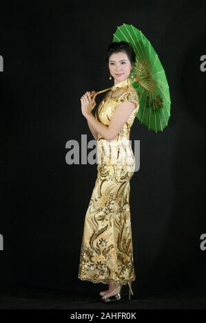 Studio shot Der asiatische Frau, stehend in entspannter Pose oder das Tragen der traditionellen Chinesischen qipao Cheongsam traditioneller Mode und halten grün Sonnenschirm Stockfoto