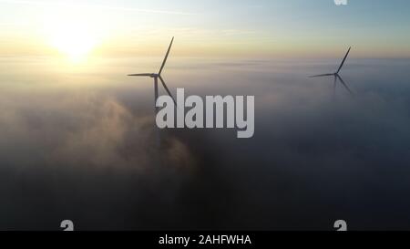 Luftbild von Windenergieanlagen bei Sonnenaufgang mit niedrigen Wolken/Nebel über dem Boden. Stockfoto