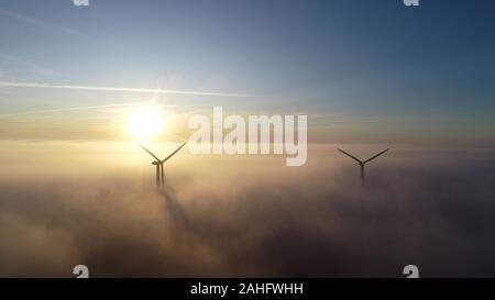 Luftbild von Windenergieanlagen bei Sonnenaufgang mit niedrigen Wolken/Nebel über dem Boden. Stockfoto