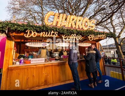 Die Princes Street Gardens, Edinburgh, Schottland, Vereinigtes Königreich. 29. Dezember 2019. Weihnachten feiern: Sonnenschein im Zentrum der Stadt bei einem Weihnachtsmarkt snack Stall verkaufen CHURROS, Donuts (Donuts) und Kaffee an Kunden Stockfoto