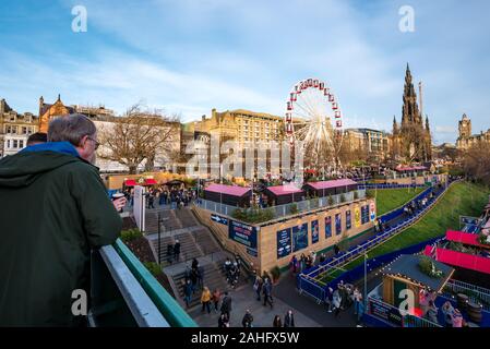 Die Princes Street Gardens, Edinburgh, Schottland, Vereinigtes Königreich. 29. Dezember 2019. Weihnachten feiern: Sonnenschein in der Innenstadt mit ein paar Suche im Blick auf die Fahrgeschäfte, Weihnachtsmarkt Stände und das Scott Monument Stockfoto