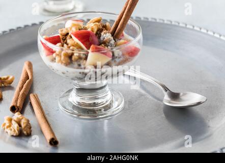 Eine Nahaufnahme Glas Schale aus Stahl geschnitten Hafer mit Chia Samen und Hanf samen vermischt und mit gehackten Äpfel, Walnüsse und Zimt gekrönt. Stockfoto