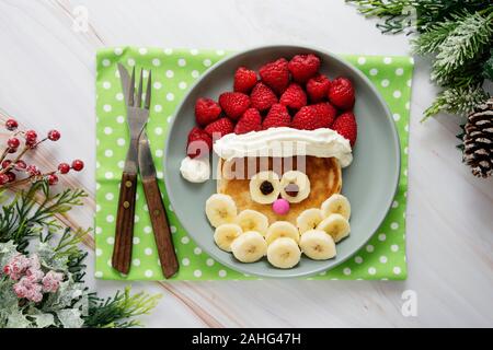 Spaß Essen für Kinder. Weihnachten Santa Pfannkuchen mit Himbeeren und Banane für Kinder Menü, Ansicht von oben mit der Kopie Platz für Text. Stockfoto