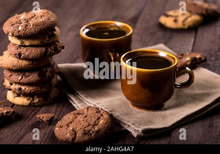 Zwei Tassen Kaffee und Chocolate Chip Cookies auf rustikalen Holzmöbeln Hintergrund. Symbolische Bild. Konzept für einen leckeren Snack. Süße Nachspeise. Stockfoto