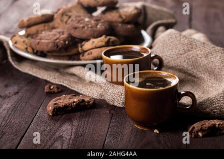 Zwei Tassen Kaffee und Chocolate Chip Cookies auf rustikalen Holzmöbeln Hintergrund. Symbolische Bild. Konzept für einen leckeren Snack. Süße Nachspeise. Stockfoto