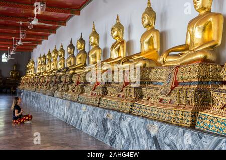 Eine Frau, die auf dem Boden sitzt und vor einer Reihe goldener buddhas meditiert Stockfoto