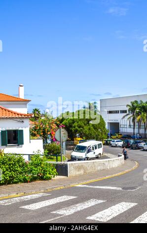 Porto da Cruz, Madeira, Portugal - Sep 24, 2019: Straße der malerischen portugiesischen Dorf auf einem vertikalen Foto. Häuser, Menschen auf der Straße, geparkte Autos. Sonnigen Tag, blauer Himmel. Stockfoto