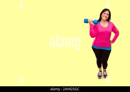 Hispanic Frau mittleren Alters in Sportklamotten halten Hantel vor einem gelben Hintergrund. Stockfoto
