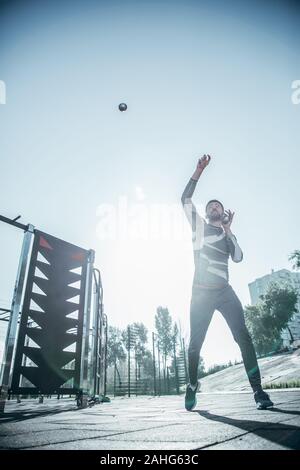 Ernster Mann springen auf den Sportplatz und fangen kleine Kugeln Stockfoto