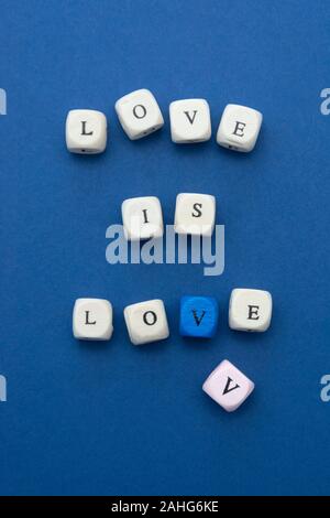 Liebe ist Liebe Nachricht auf Holzklötze auf blauem Hintergrund geschrieben, Ansicht von oben. Stockfoto