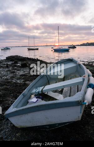 Ein hölzernes Boot am Ufer bei Ebbe mit Segelbooten auf dem Wasser im Hintergrund bei Sonnenuntergang, Gosport, Hampshire, Großbritannien Stockfoto