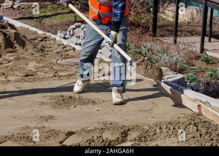 Ein Arbeiter mit einer Schaufel Sand trägt die Stiftung unter der Pflastersteine. Stockfoto