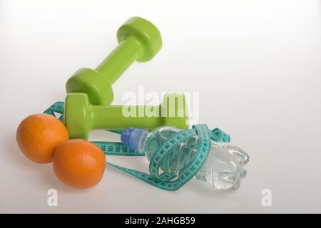 Sport und gesunde Regime, kopieren. Hanteln in grüner Farbe, Flasche Wasser, Maßband und Obst auf weißem Hintergrund. Barbells aus Kunststoff in der Nähe von saftigen Orangen. Diät und Sport regime Konzept Stockfoto