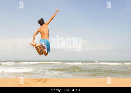 Junger Mann, der einen akrobatischen Sprung am leeren Strand in Bentota, Sri Lanka unternimmt. Freedom, Sommer Reise Abenteuer Konzept Stockfoto