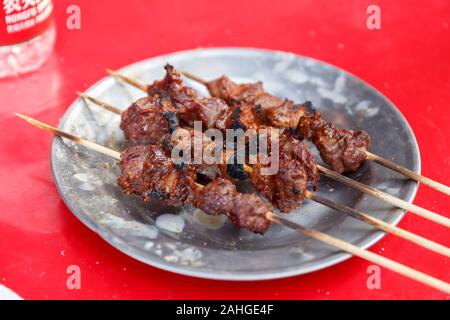 Vier gegrillte Lammspieße, auf einem Teller serviert und bereit zum Essen. Typische Küche in Xinjiang - als Straßennahrung oder in Restaurants serviert. Stockfoto