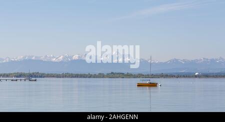 Panoramasicht auf den Ammersee mit orangefarbenem segelboot und Wettersteingebirge im Hintergrund. Der schneebedeckte Gipfel in der Mitte ist Zugspitze. Stockfoto
