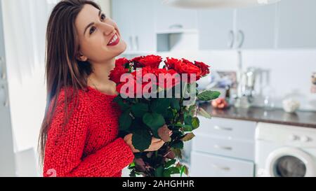 Valentines Tag. Junge Frau gefunden Strauß roter Rosen auf Küche. Glückliches Mädchen mit Blumen. Stockfoto