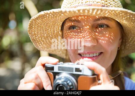 Nahaufnahmen einer schönen Frau im Strohhut travelig in tropischem Wald, Fotos mit Retro-Kamera. Helle Schatten durch ausgeschnittene Details Stockfoto