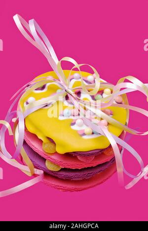 Stapel buntes Osterfest cookies mit Süßigkeiten besprüht und pastellfarbenen Bänder in einer Schleife gebunden. Der Hintergrund ist strukturierte rosa Material. Stockfoto