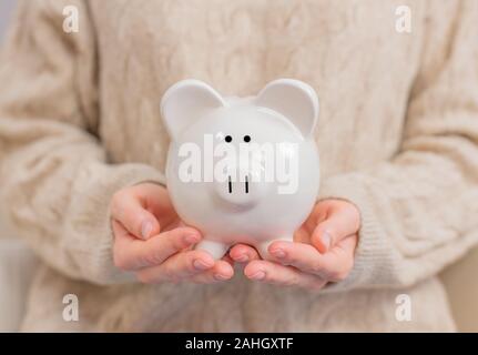 Frau hält piggy Bank in den Händen. Frau macht Einsparungen setzt Geld in ein Sparschwein. Stockfoto