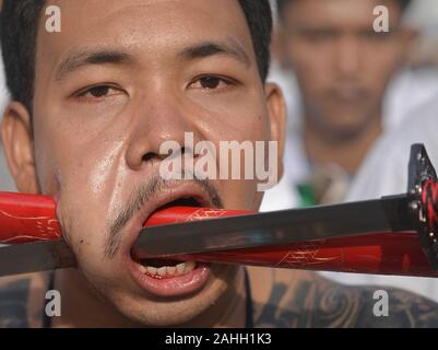 Junge Thai Chinesische taoistische Anhänger durchdringt seine Wange mit der Klinge und Scheide eines asiatischen Schwert während der neun Kaiser Götter Festival. Stockfoto