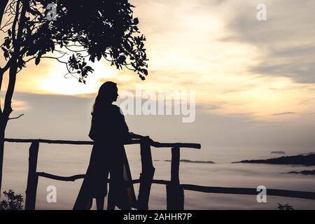 Trang, Thailand - 11. Mai 2018: Silhouette Dame stand halten Balkon vor der Blick auf die Hügel von Ozean Nebel im Morgengrauen Zeit Stockfoto