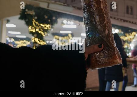 Hand mit ungarischen Spezialitäten Kurtoskalacs - Schornstein Kuchen Gebäck. Saisonal Spieß kuchen Freude am Weihnachtsmarkt in Budapest Ungarn verkauft. Stockfoto