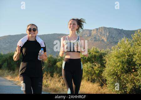 Zwei laufenden Frauen. Mutter und Tochter teenager Laufen draußen auf der Straße in den Bergen im Sommer sonnigen Tag. Familie, gesunden, aktiven Sport Lifestyle. Stockfoto