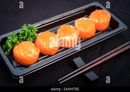 Sashimi Brötchen mit Fisch Eier oben dienen in schwarzem Kunststoff Platte mit Essstäbchen auf schwarz Tischdecke Stockfoto