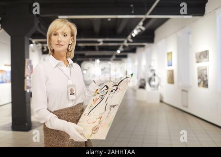 Taille bis Portrait von eleganten reife Frau präsentiert Malerei, während in der Kunst Galerie oder einem Museum arbeiten, kopieren Raum Stockfoto