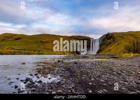 Skogafoss Wasserfall aus der Ferne mit unkenntlich Besucher, mit einer teilweise bedecktem Himmel am Ende eines frühen Oktober Nachmittag gesehen, Island Stockfoto