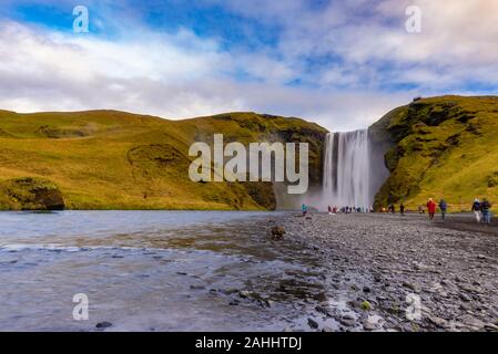 Skogafoss Wasserfall aus der Ferne mit unkenntlich Besucher, mit einer teilweise bedecktem Himmel am Ende eines frühen Oktober Nachmittag gesehen, Island Stockfoto