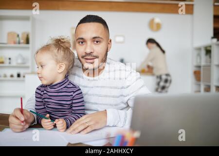Portrait von gemischten liebevolle Rasse Vater auf Kamera beim Zeichnen von Bildern mit niedlichen kleinen Mädchen zu Hause, Kopie Raum Stockfoto