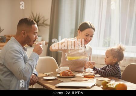In warmen Tönen Porträt des modernen Happy Family Mit Frühstück zu Hause sitzen am Küchentisch im Sonnenlicht Stockfoto