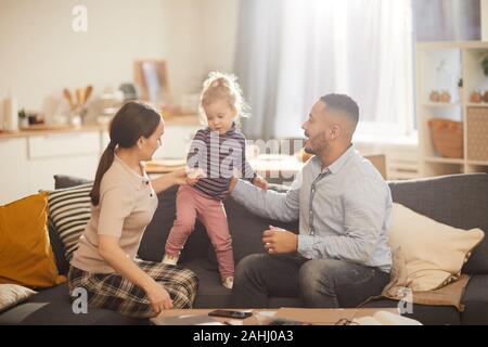 In warmen Farbtönen Portrait von glücklich moderne Familie spielen mit niedlichen kleinen Tochter im lichtdurchfluteten Interieur, kopieren Raum