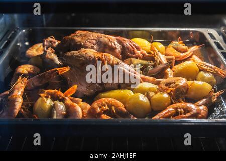 Kid Fleisch im Ofen gebacken mit Kartoffeln, Garnelen, Garnelen und Gemüse. Familie Veranstaltung und sammeln Abendessen mit leere Raum. Stockfoto