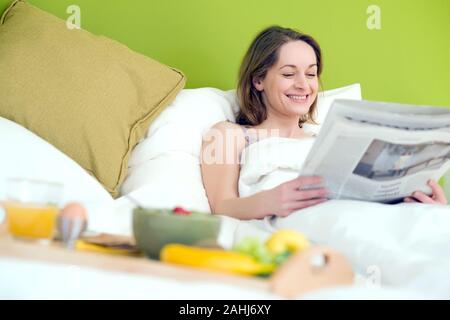 25 -30 jährige Frau schläft im Bett und liest die Zeitung, HERR: Ja Stockfoto