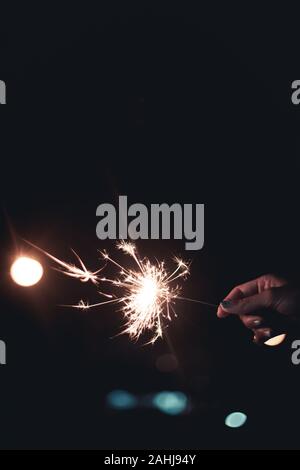 Woman's Hand wunderkerzen Stick auf Feuer, Flamme lange Licht mit Bokeh der Glühlampe in der Nacht die Zeit verteilen auf schwarzem Hintergrund Stockfoto