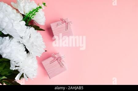 Zwei rosa Geschenkkarton mit goldenen Schleife. Blumenstrauß aus den weißen Blüten. Gifting elegantes Konzept auf rosa Hintergrund, mit kopieren. Stockfoto