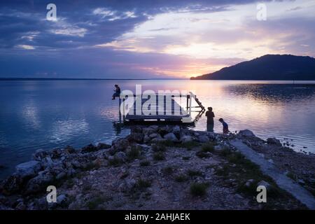 Sihouettes von Menschen entlang Pier mit orange Sonnenuntergang auf dramatische violett blau Himmel entlang des Lake Itza, El Remate, Peten, Guatemala Stockfoto