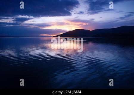 Orange Sonnenuntergang am schönen lila blauem Himmel entlang des Lake Itza mit dramatischen Wellen, El Remate, Peten, Guatemala Stockfoto